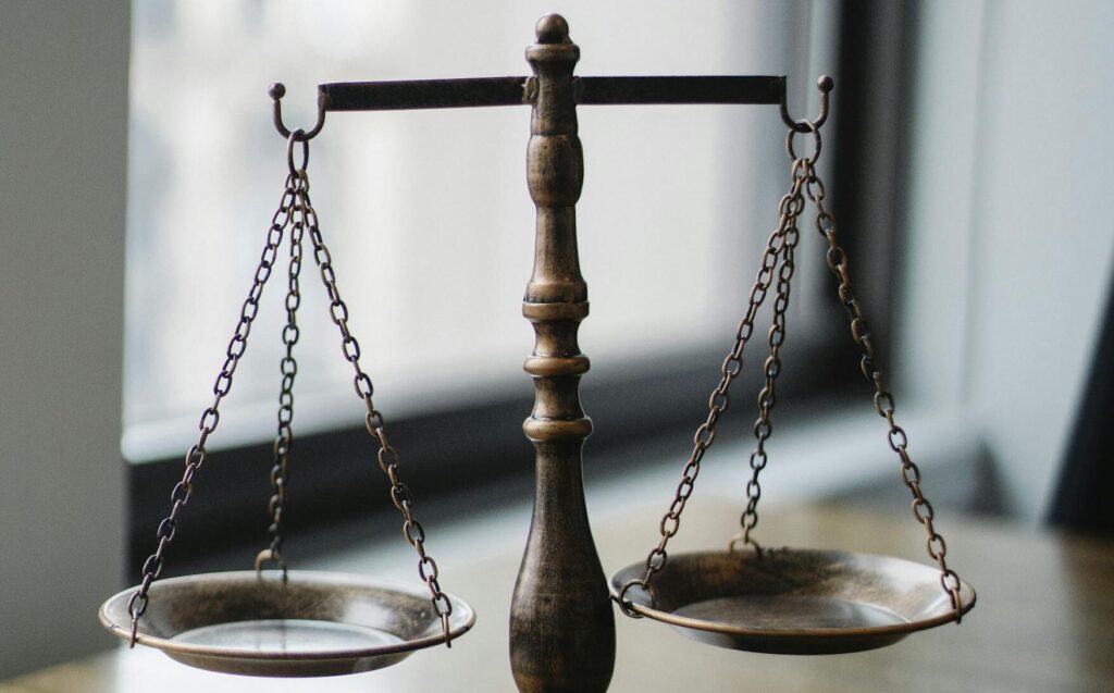 Decorative judgement scale and gavel placed on desk in light lawyer office against window